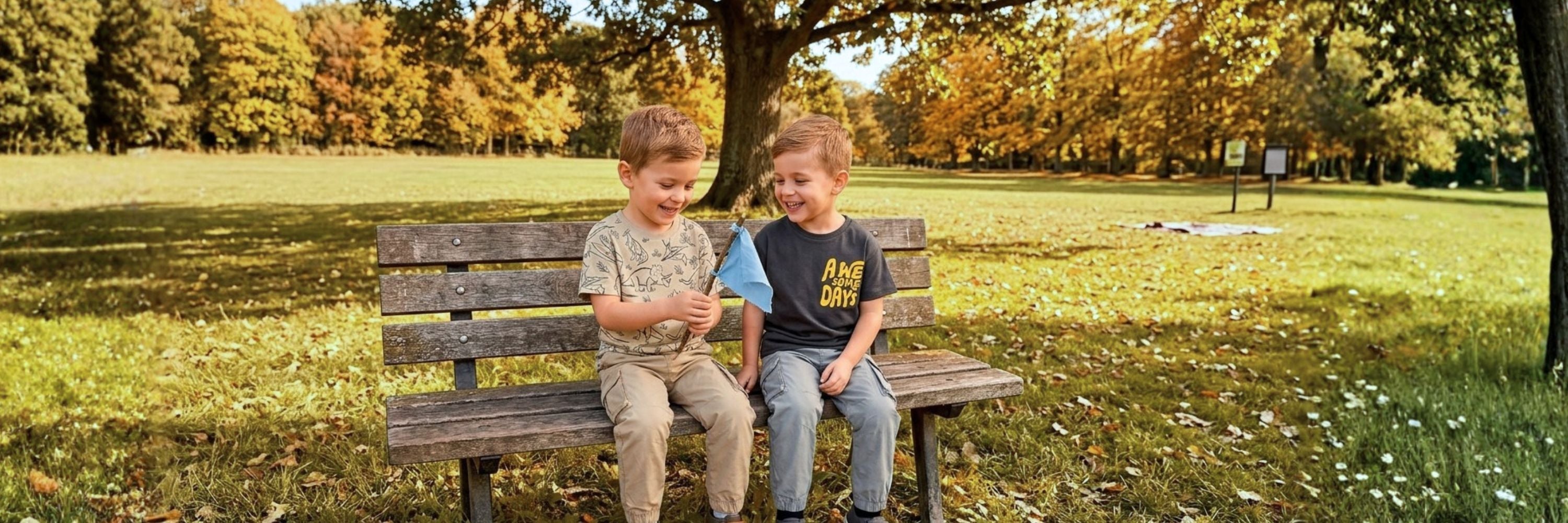 Two boys laughing while sitting on a park bench, wearing casual t-shirts and cargo-style trousers.