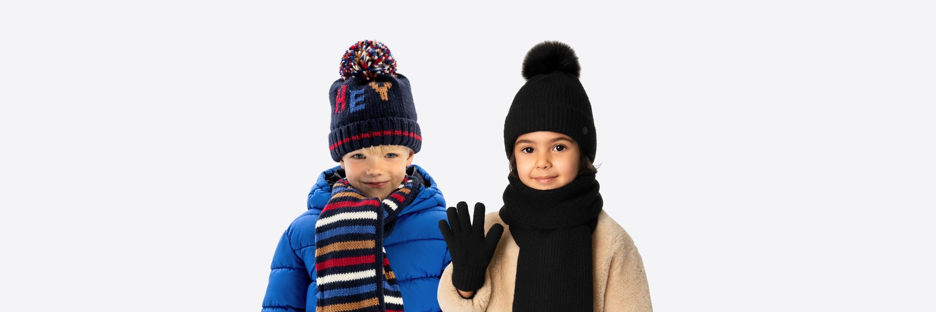 Two children wearing winter accessories, including hats with pom-poms, scarves, and gloves, posed against a plain white background.