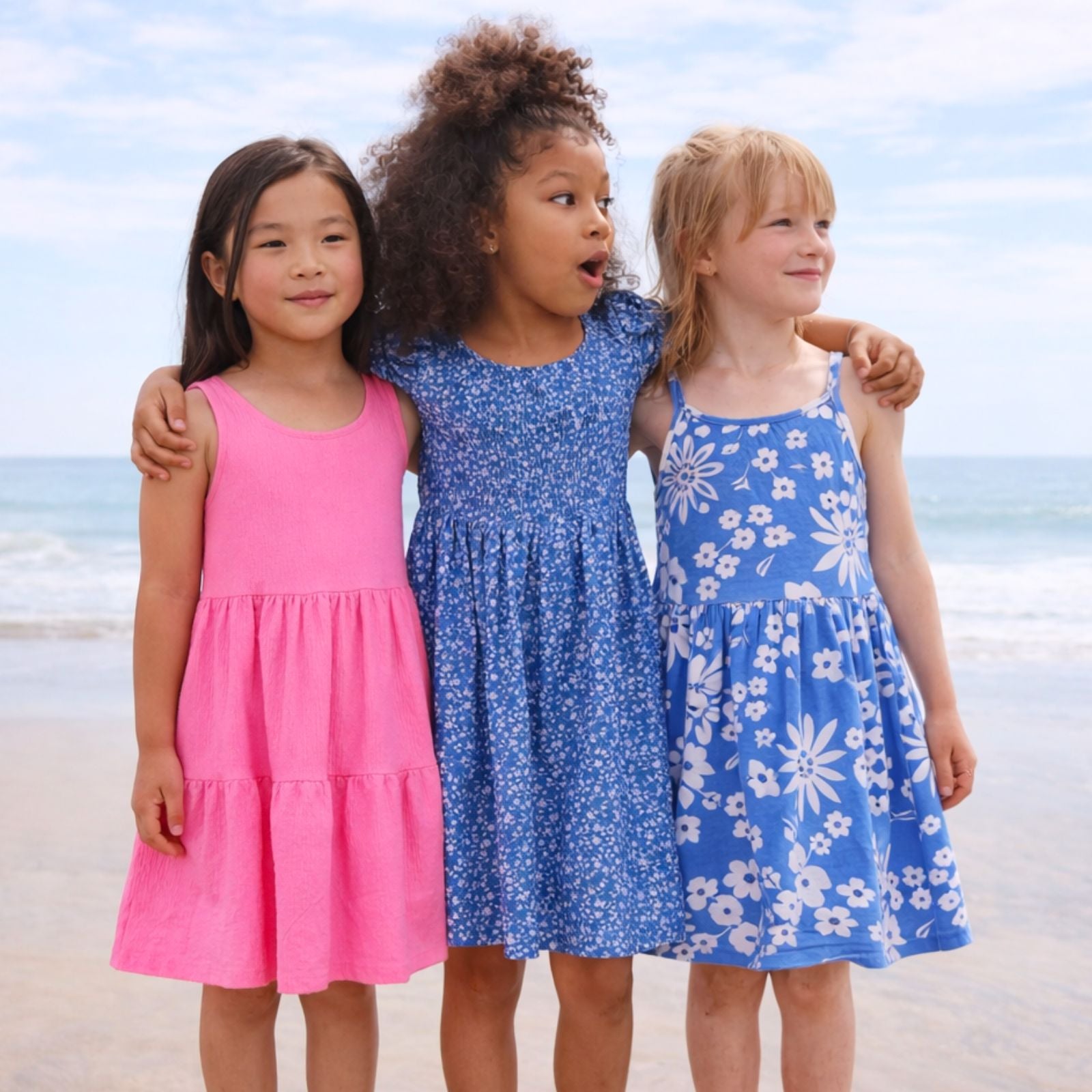 Three children in colorful dresses standing on a beach.