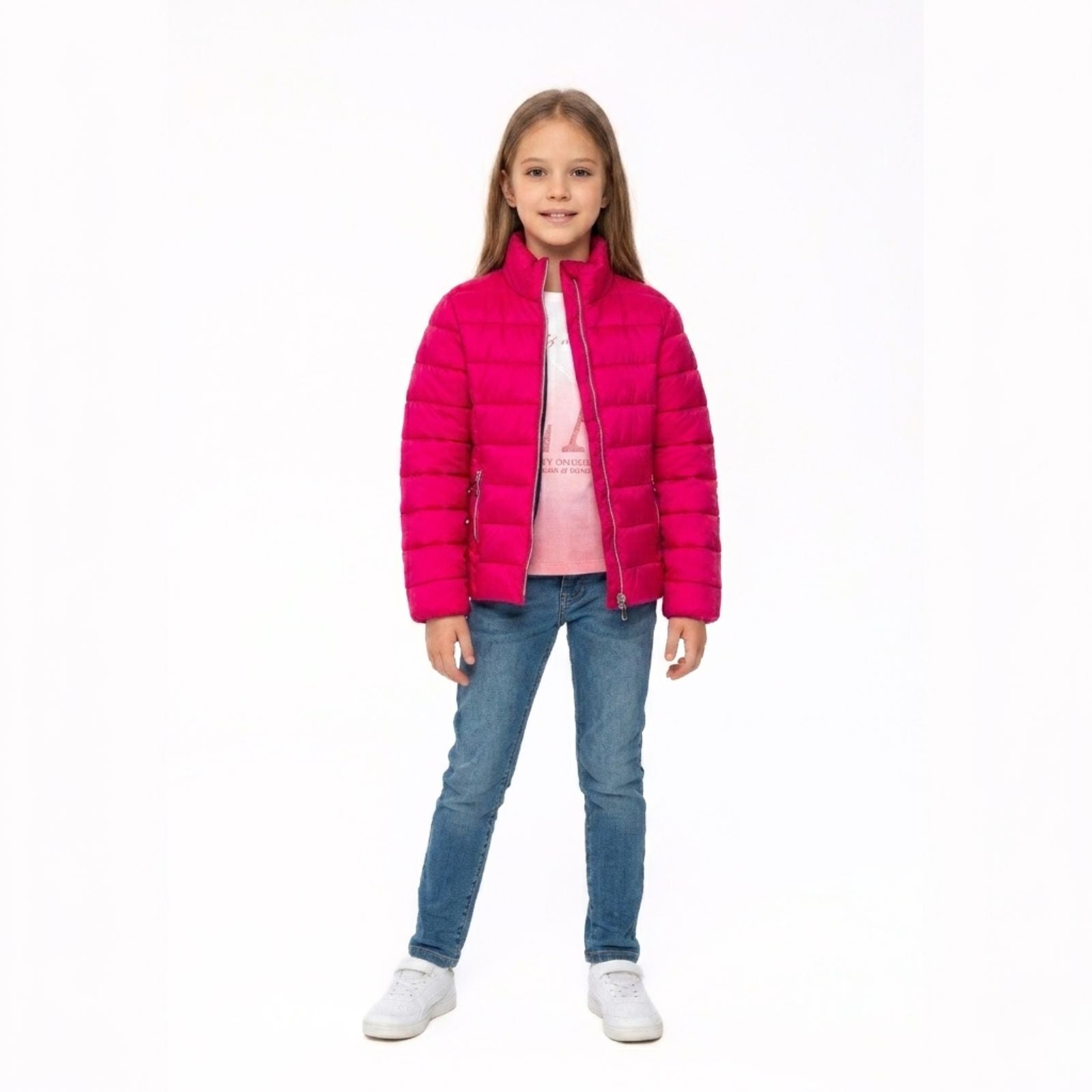Girl wearing bright pink quilted padded jacket over pink top and blue jeans, standing against white background.