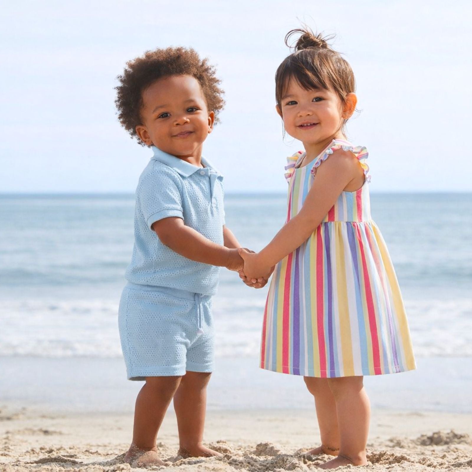 Two children holding hands on a beach with ocean in the background