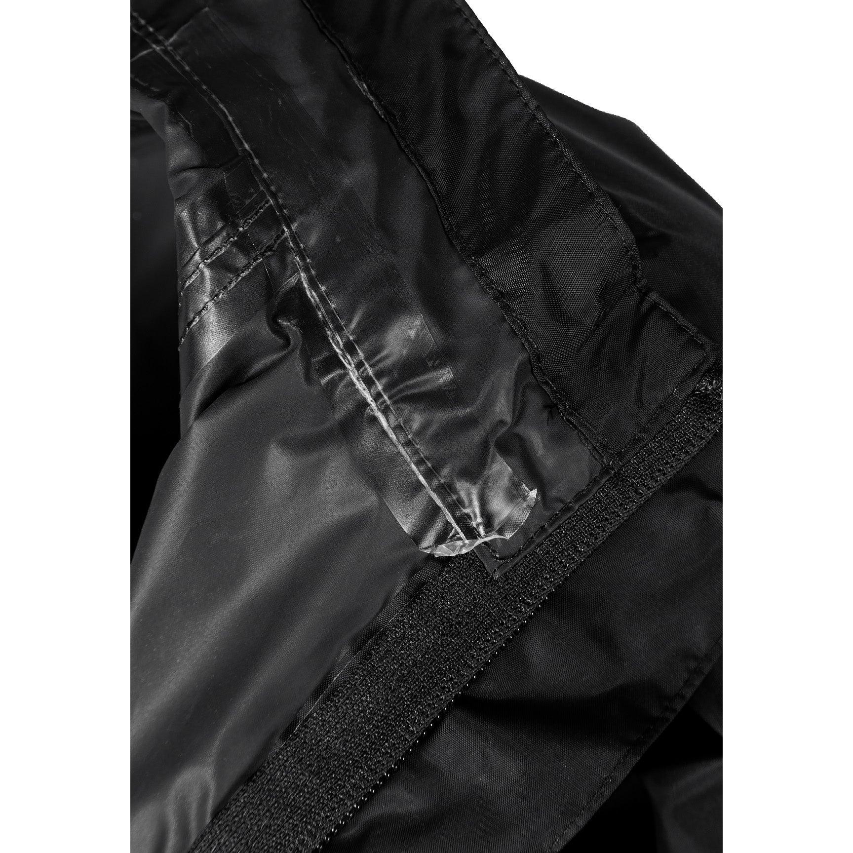 Boy in black hooded waterproof jacket pointing forward, wearing light blue cargo jeans and black sneakers on white studio background