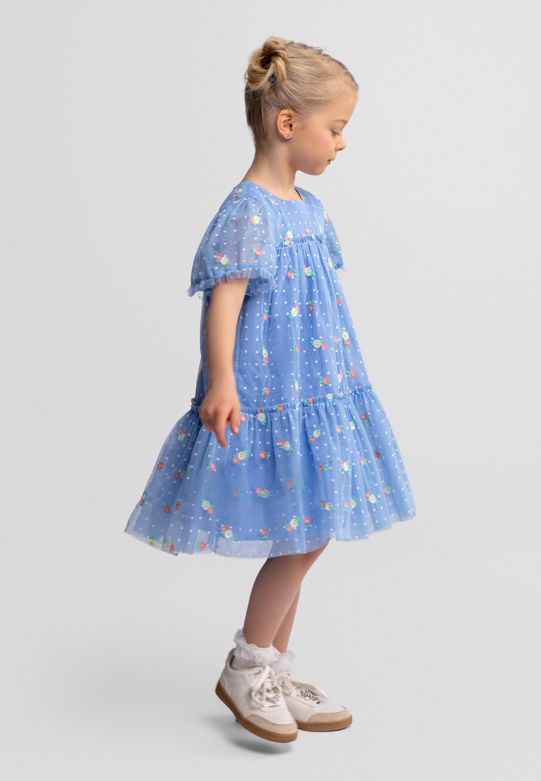 Side view of blue tulle dress showing button fastening, tiered layers and floral dot pattern on white background