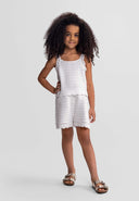 Young girl wearing a white outfit with a textured pattern on a plain background