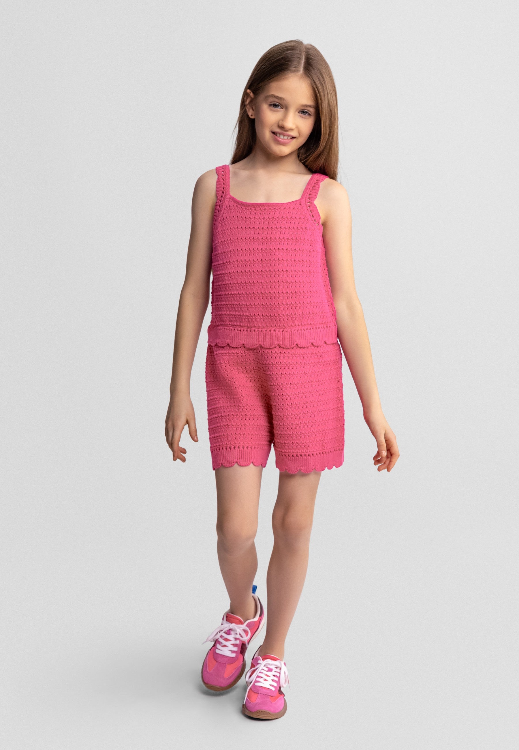 Young girl wearing a pink crochet outfit on a light gray background