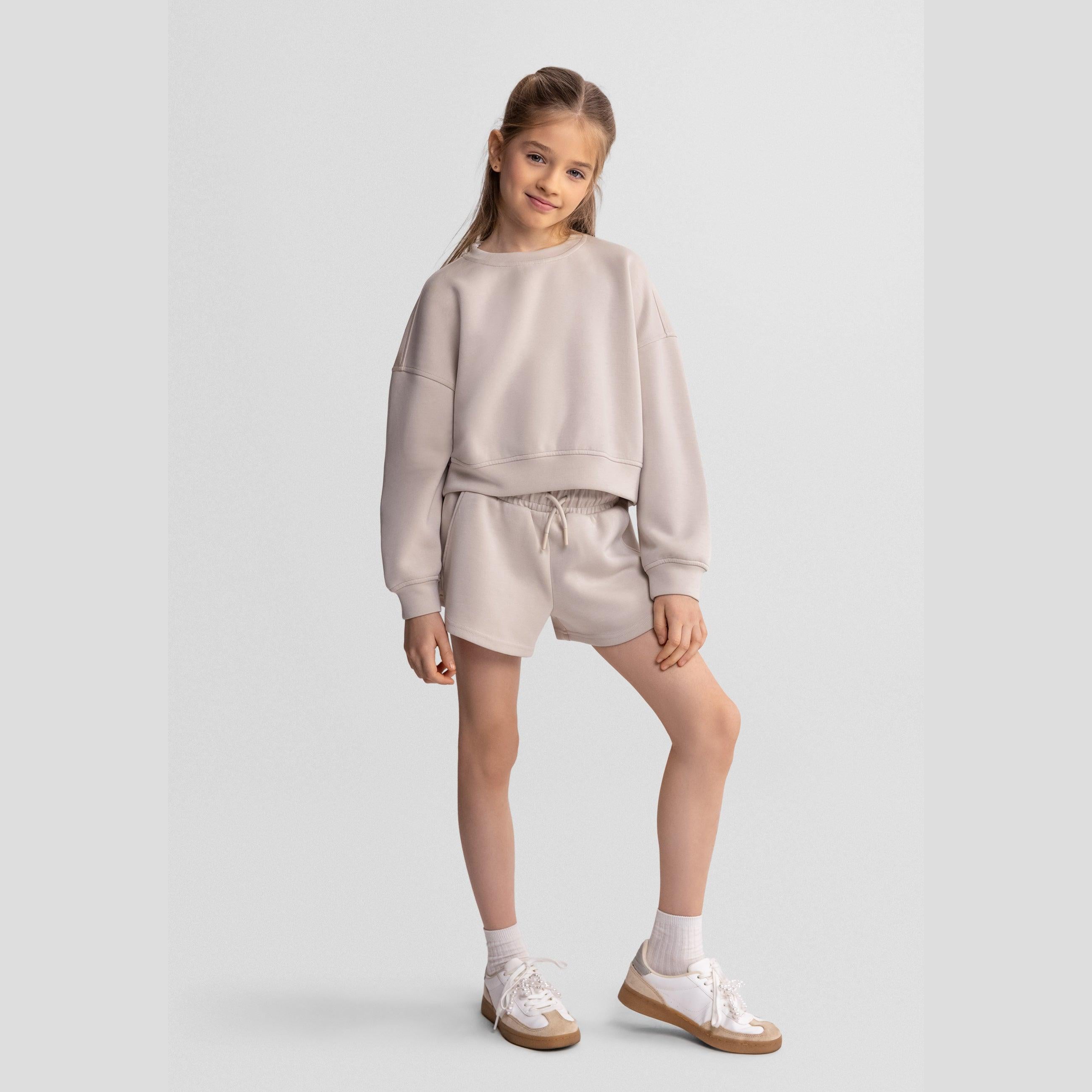 Close-up detail of beige shorts showing elasticated waistband with drawstring ties on neutral background