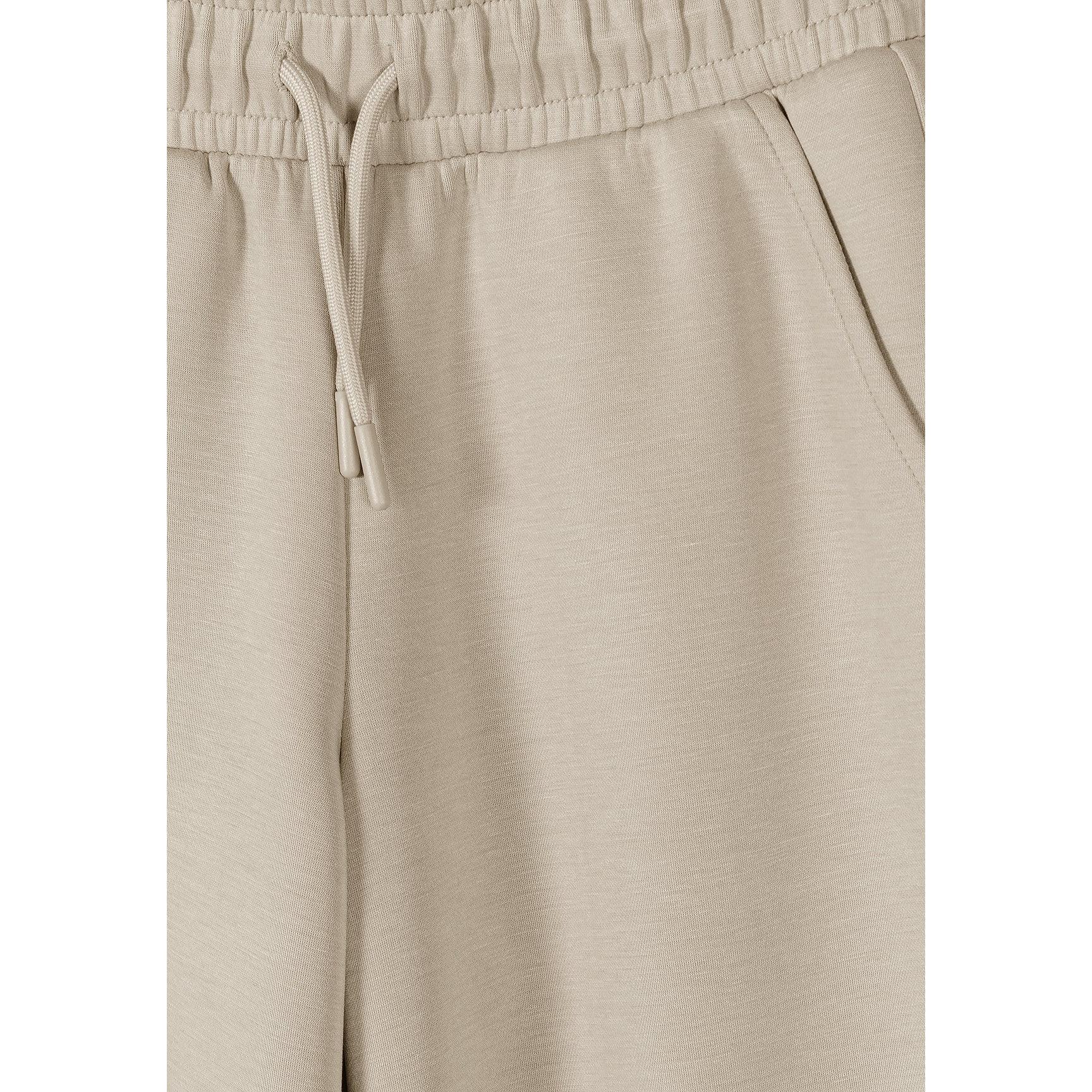 Close-up detail of beige joggers showing elastic waistband with drawstring and front pocket construction