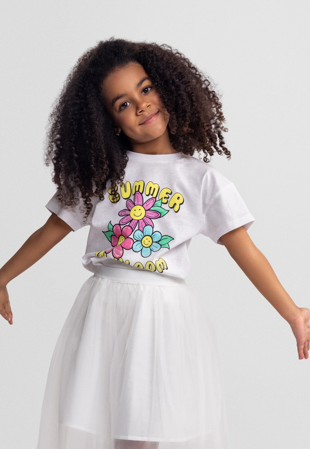 Child wearing a white t-shirt with colorful graphics and text, standing against a plain background