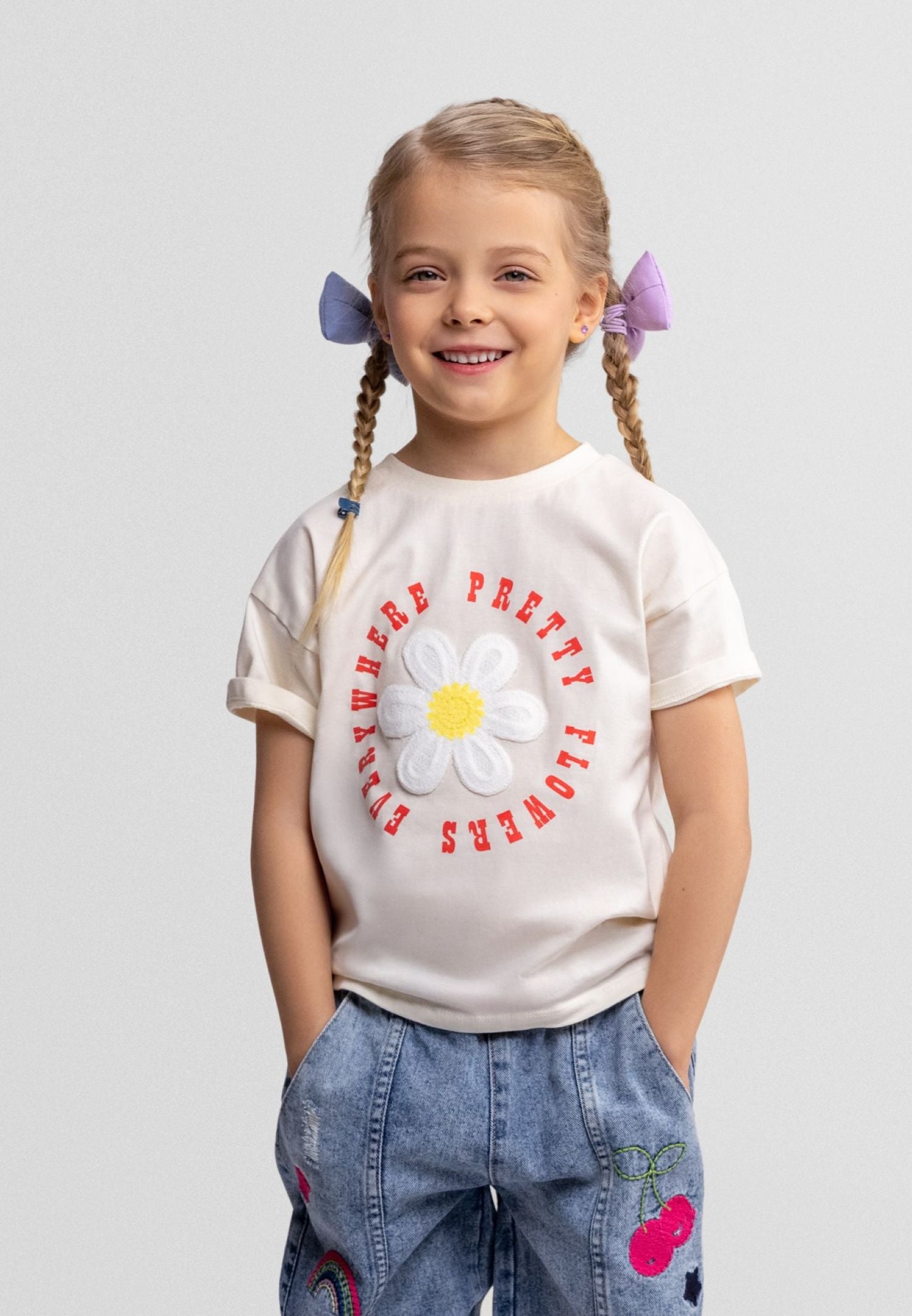Young girl wearing a white t-shirt with a flower graphic and text on a plain background