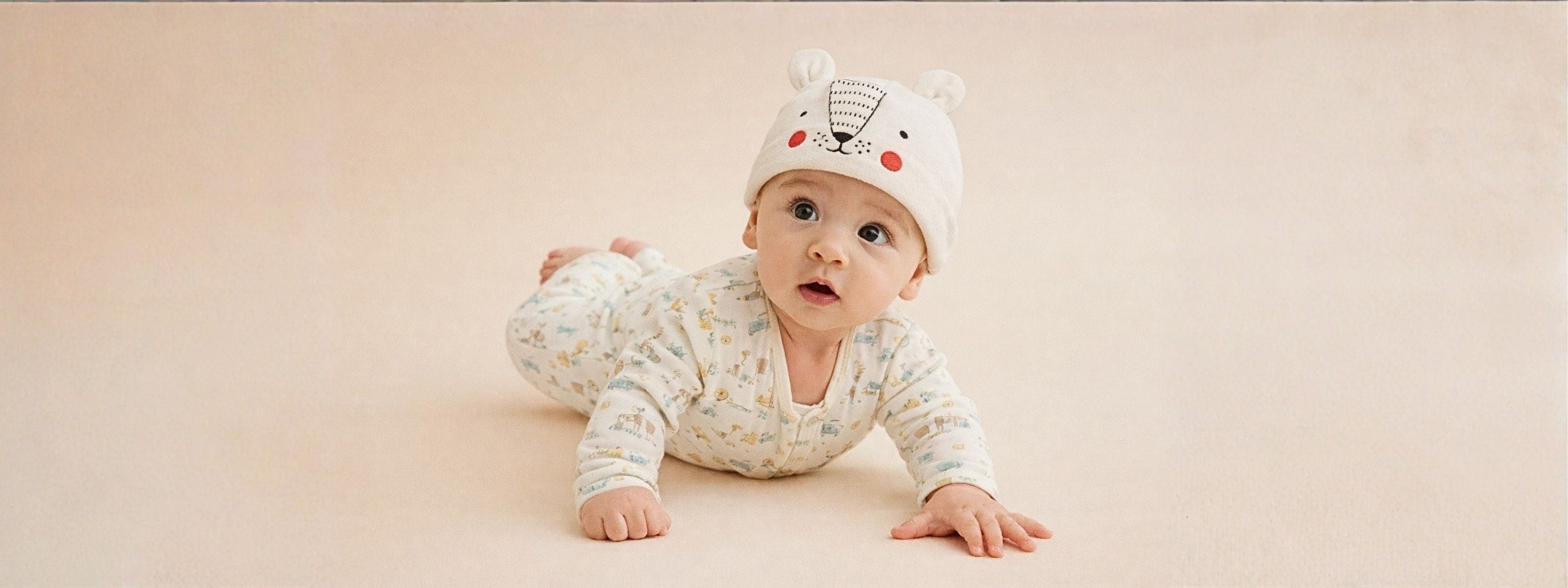 Baby wearing a patterned outfit and a white hat with animal ears on a beige background