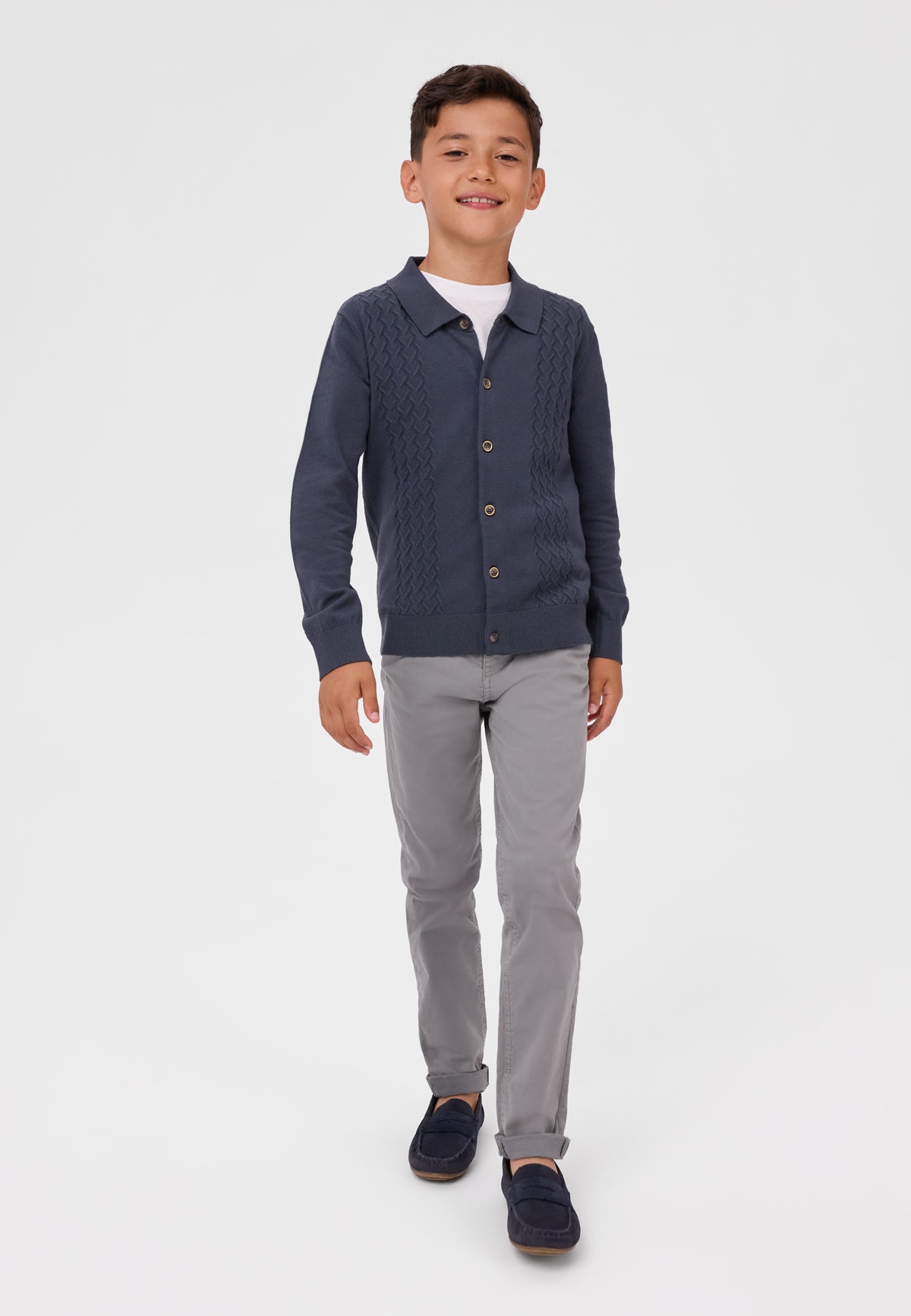 Boy walking in grey chinos with rolled ankles, navy cardigan and dark loafers.