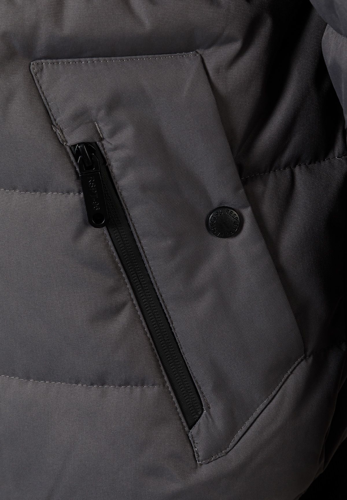 Detail of a grey padded jacket showing a zippered pocket and logo badge.