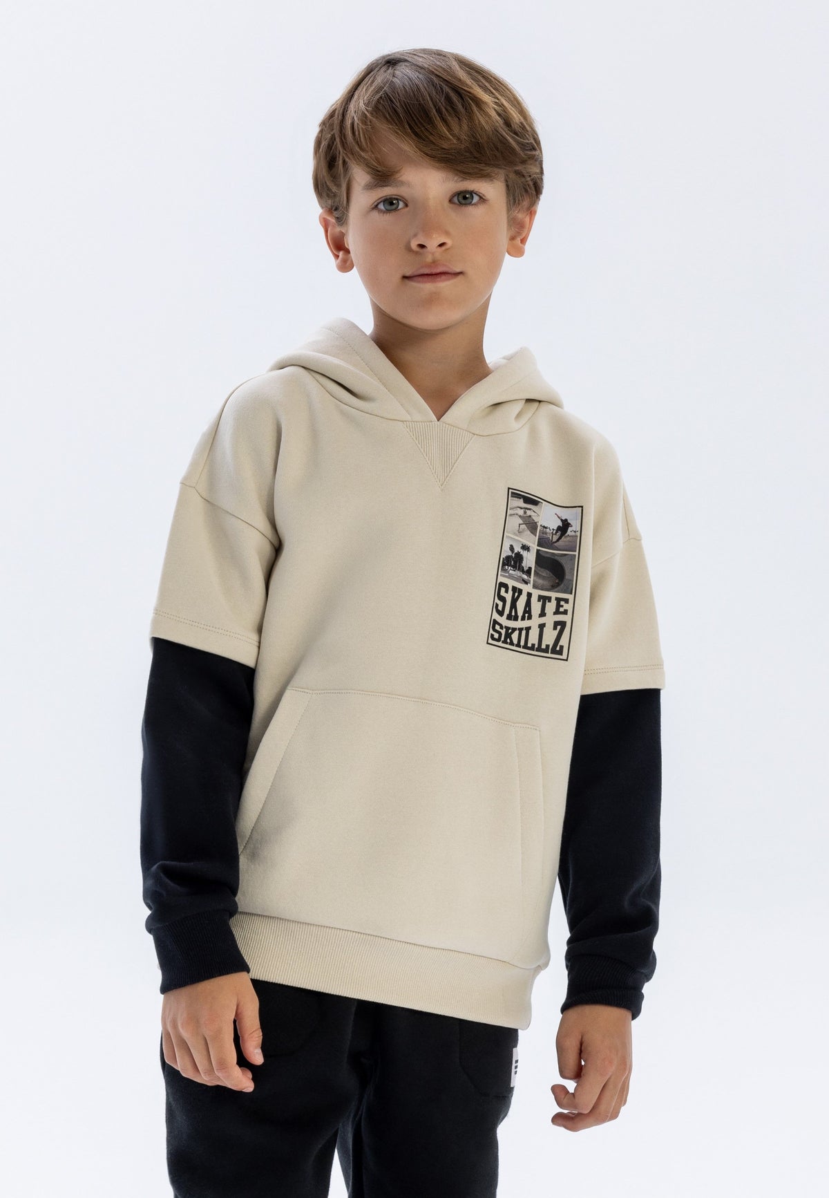Boy wearing light stone hooded sweatshirt with black lower sleeves and Skate Skillz chest graphic.