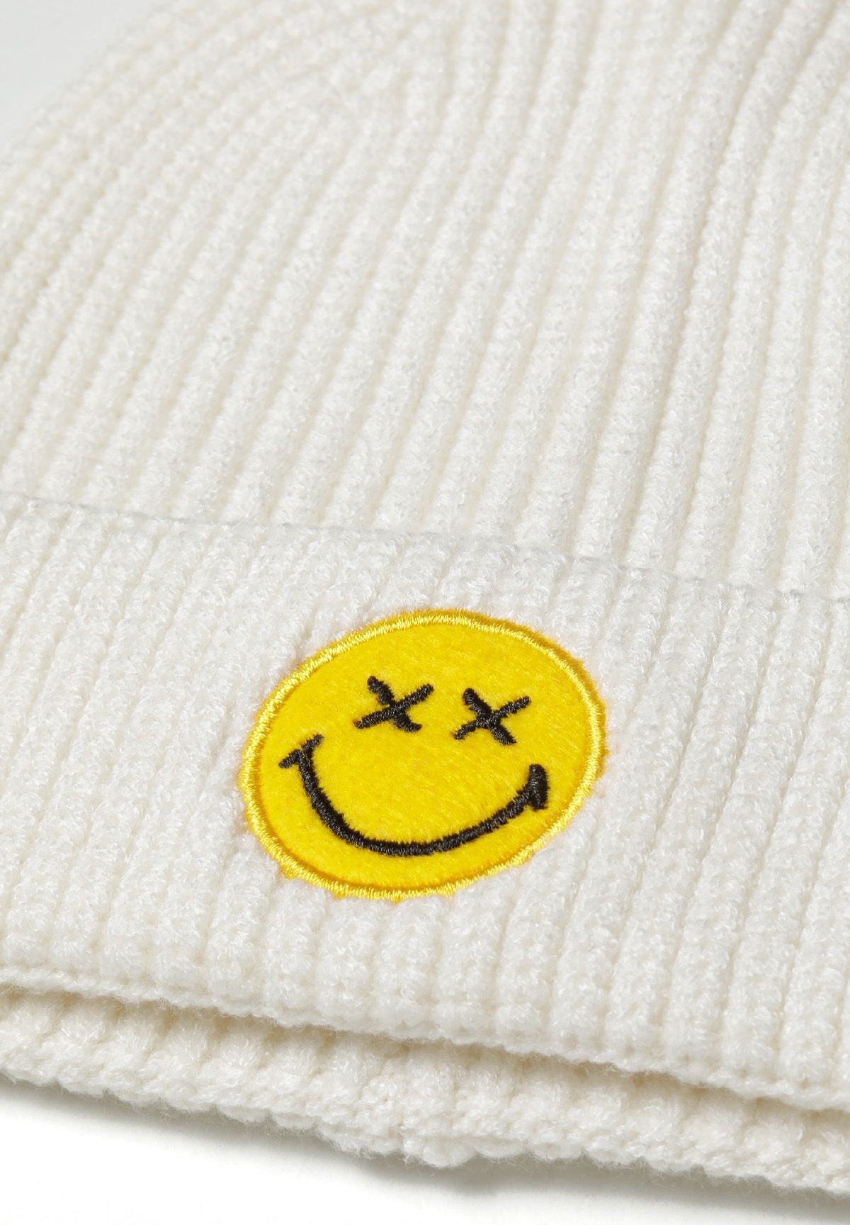 Cream ribbed beanie, smiley patch detail.