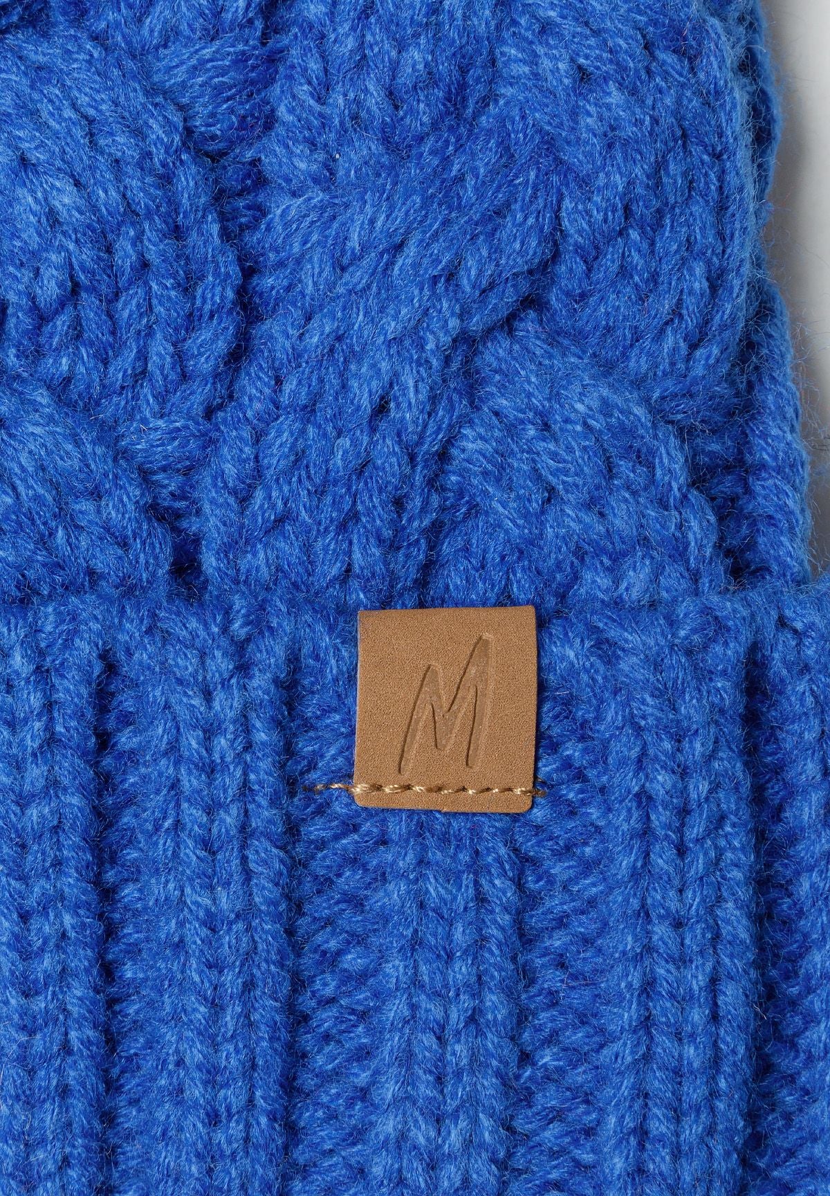 Detail of a cobalt blue knitted boys hat with cable knit pattern and a stitched tab.
