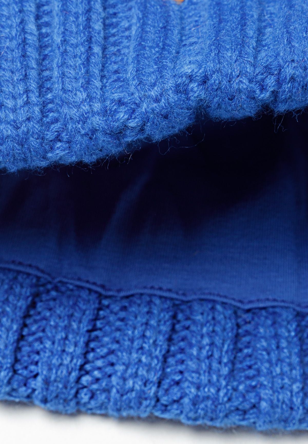Detail of a boys knitted pom pom hat in cobalt blue with cable knit texture.