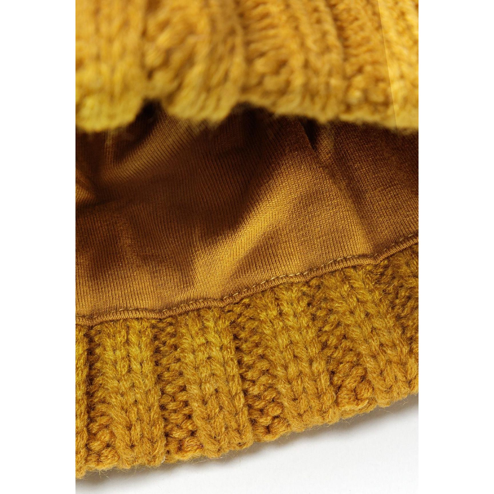 Interior view of mustard beanie showing soft brown fleece lining and ribbed edge construction detail with cable knit exterior visible