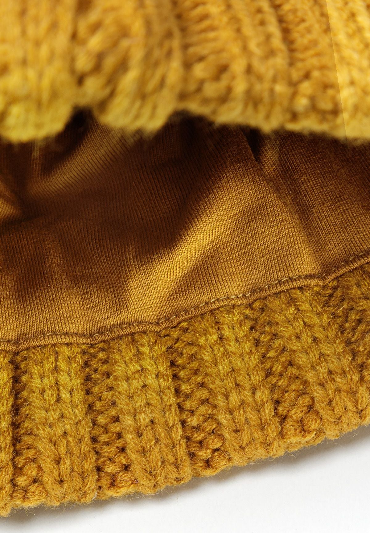 Detail of a mustard knitted cable hat with a pom pom and ribbed edge.