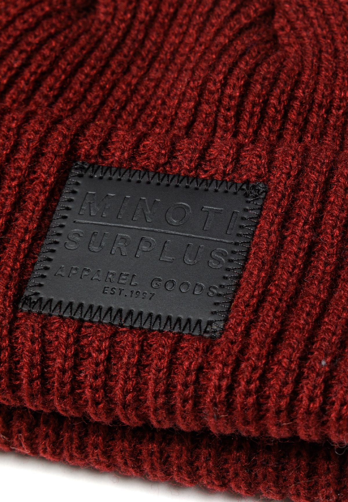Detail of a knitted fisherman hat in dark red with a black logo badge.
