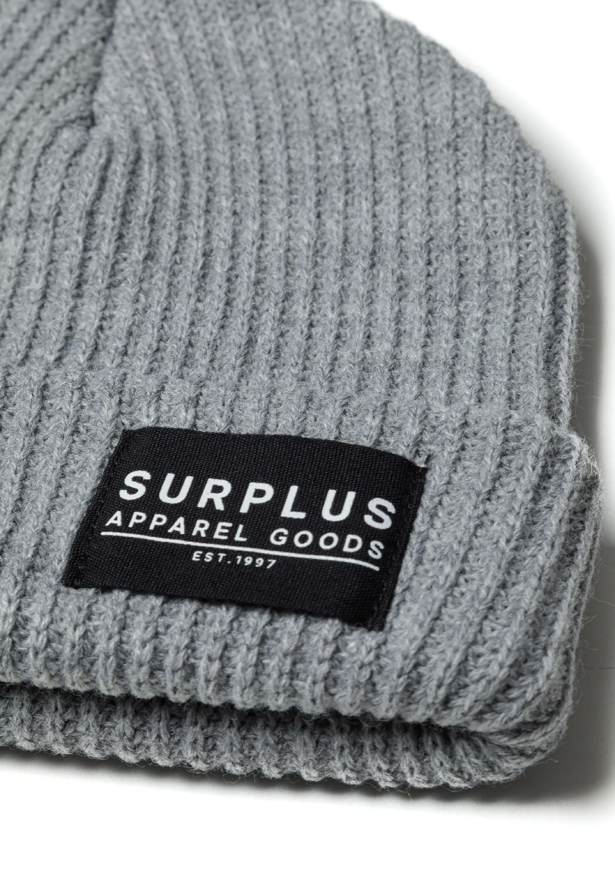 Detail of a rib knitted grey hat with a logo badge.