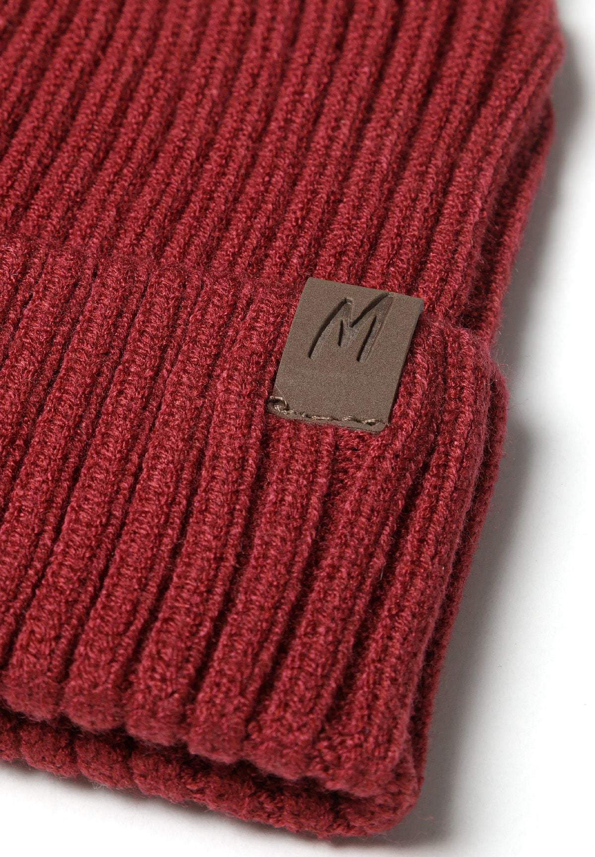 Detail of a ribbed knit hat in dark red with a tab detail on the cuff.