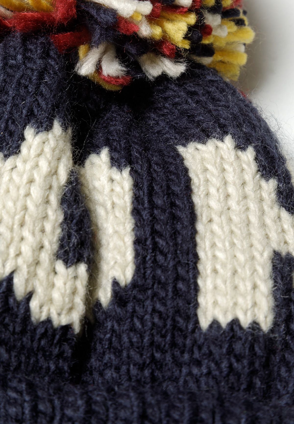 Close-up of a boys jacquard hat in navy with a playful pom pom and knitted pattern.
