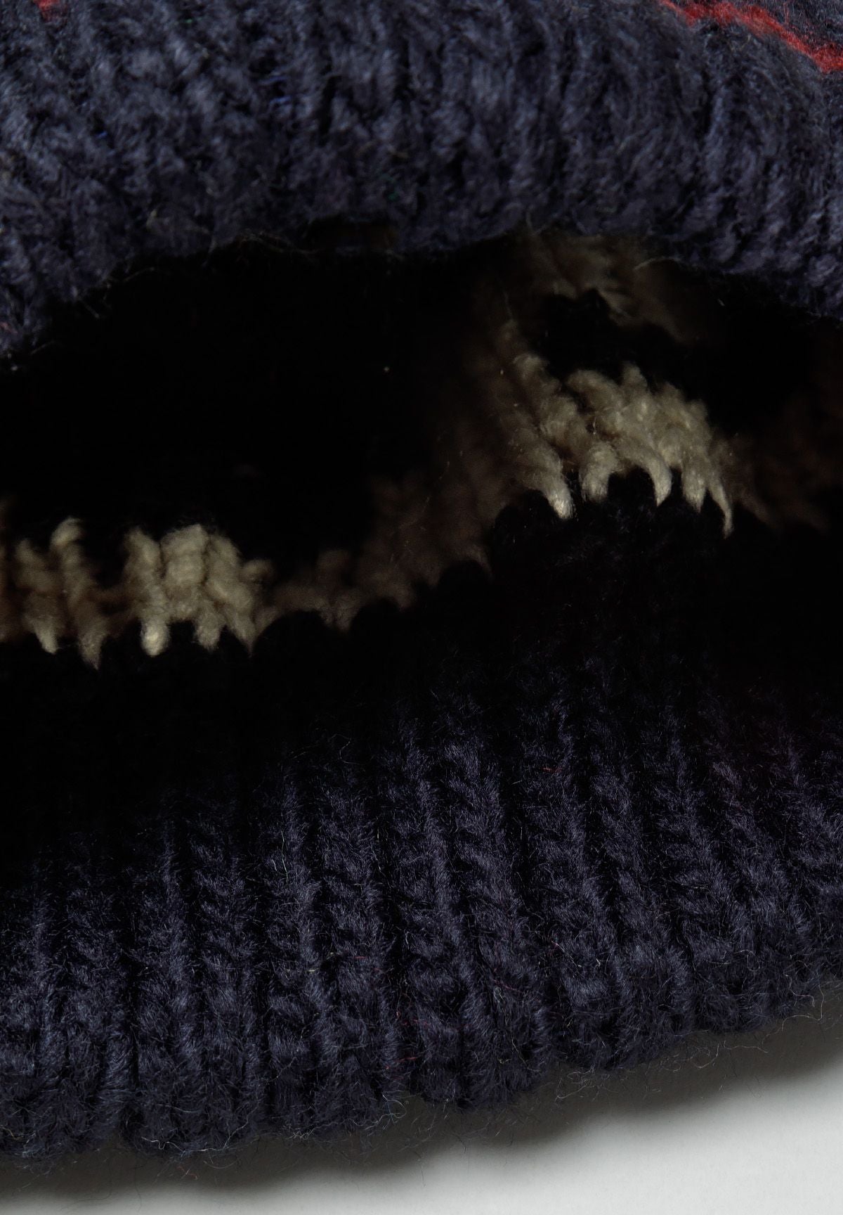 Close-up of a boys jacquard hat in navy with a pom pom and textured knit pattern.
