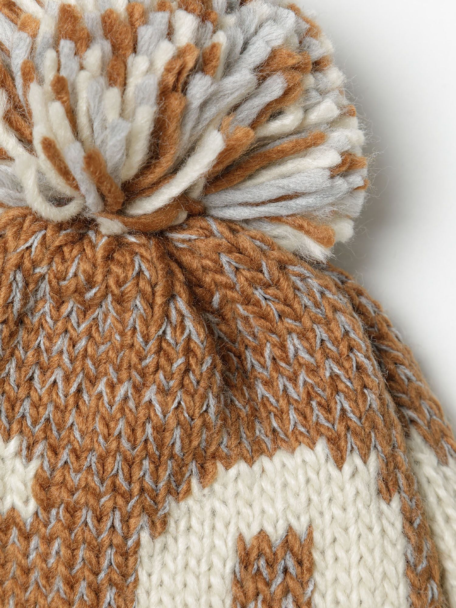 Close-up of a boys jacquard hat in beige with a pom pom and textured patterns.
