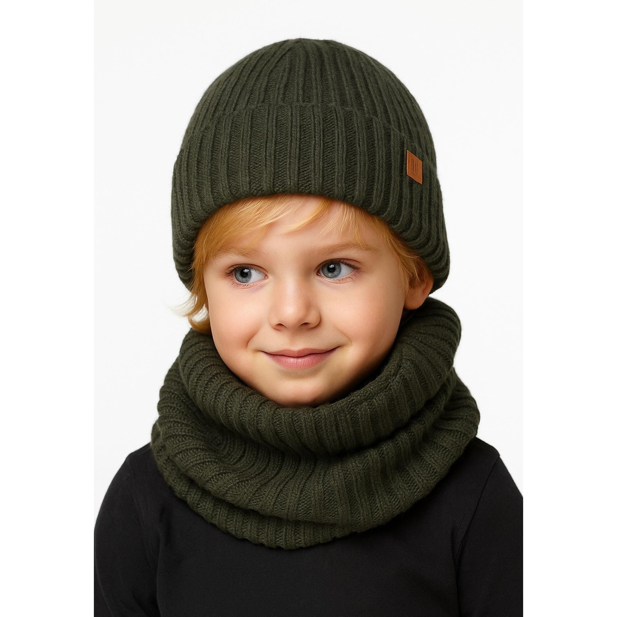 Young child wearing khaki ribbed knit beanie and matching snood over black top, smiling at camera against white background