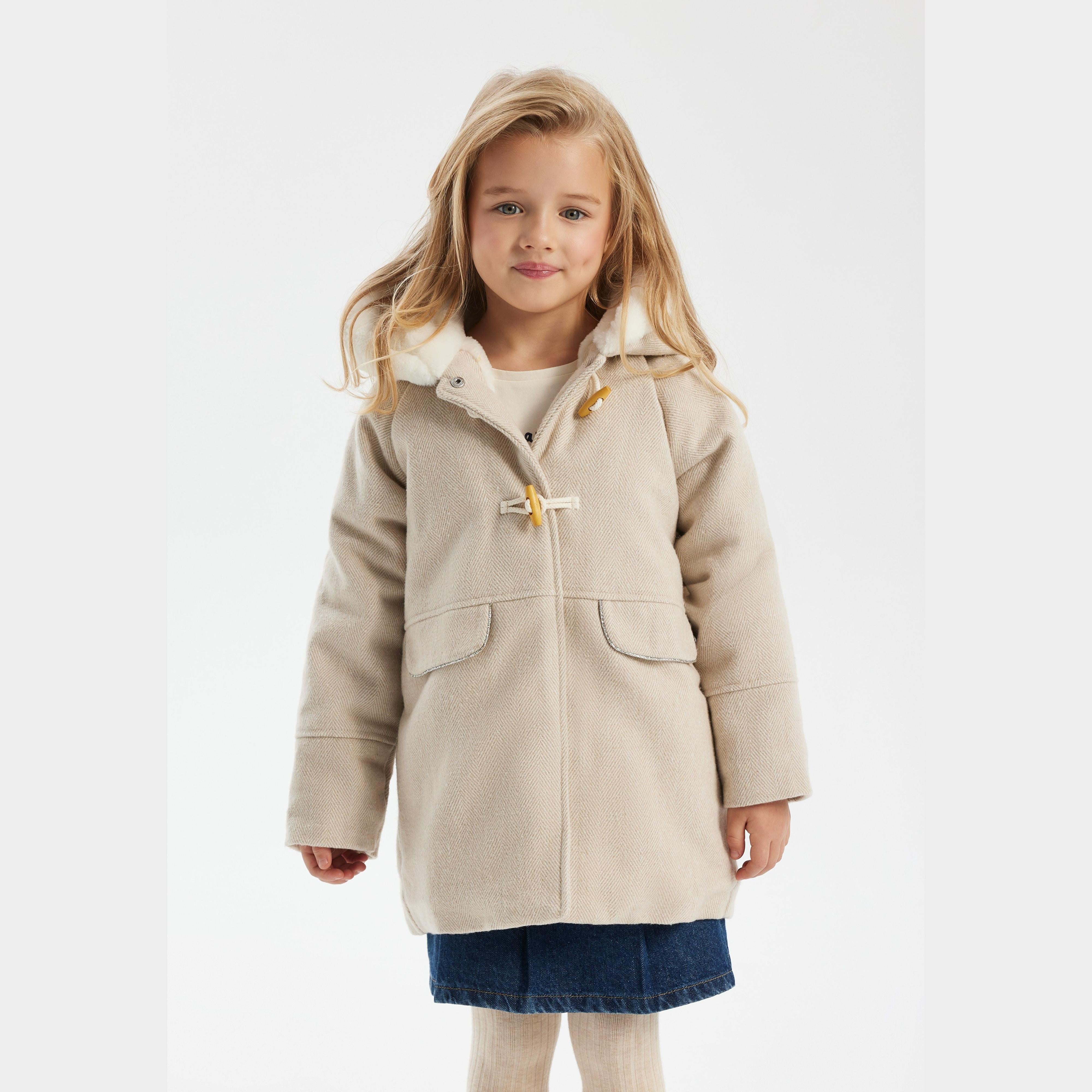 Young girl wearing grey wool blend winter coat with faux fur hood, toggle fastenings and front pockets, paired with denim skirt and cream tights on white background