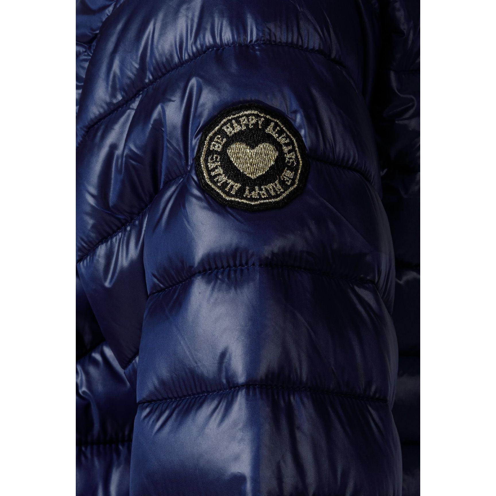 Close-up detail of navy quilted jacket showing circular embroidered badge with heart design and text on padded sleeve