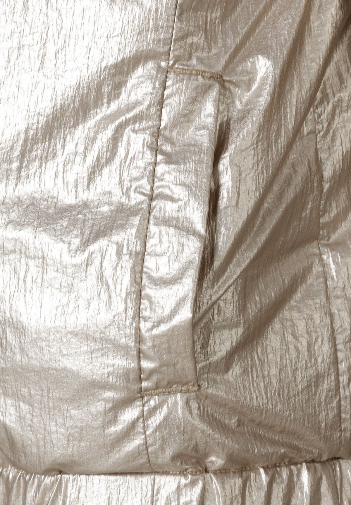 Detail of a girls reversible jacket with a metallic beige exterior and a side pocket.