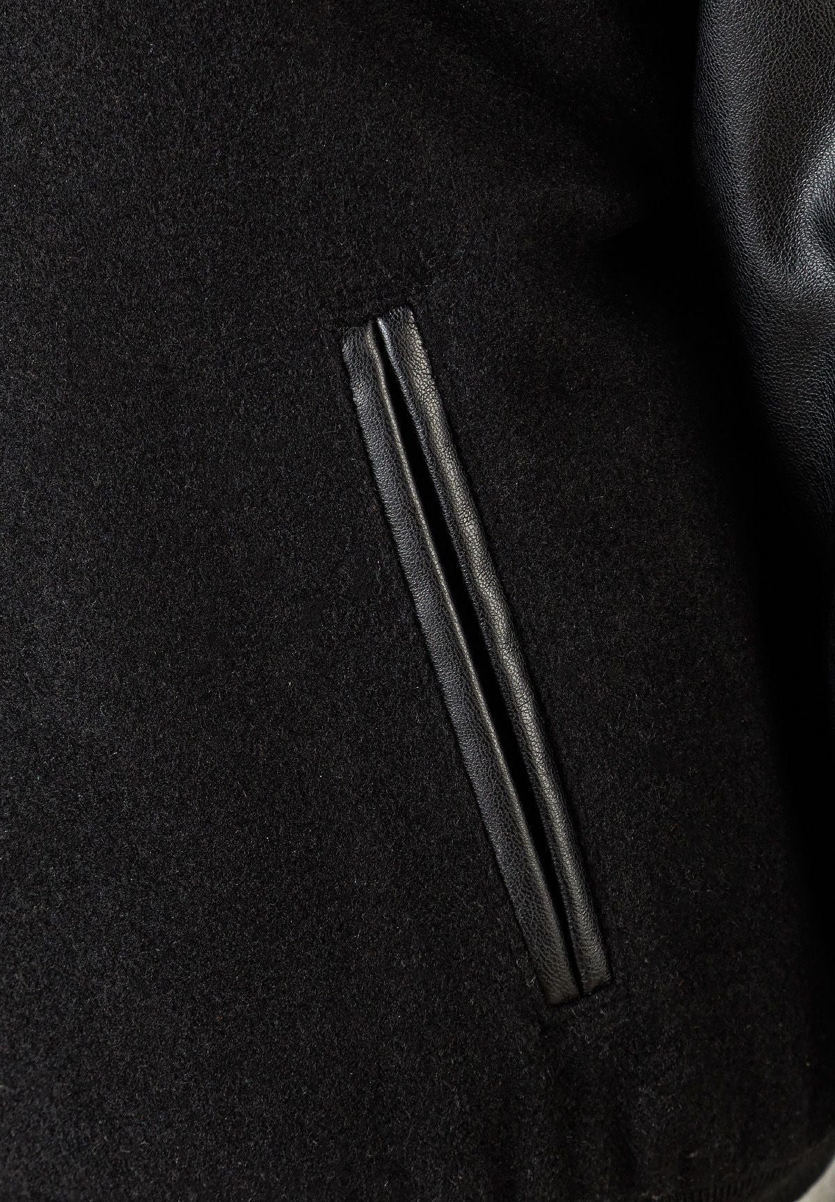 Detail of a boys baseball jacket showing black faux leather and felt fabric.