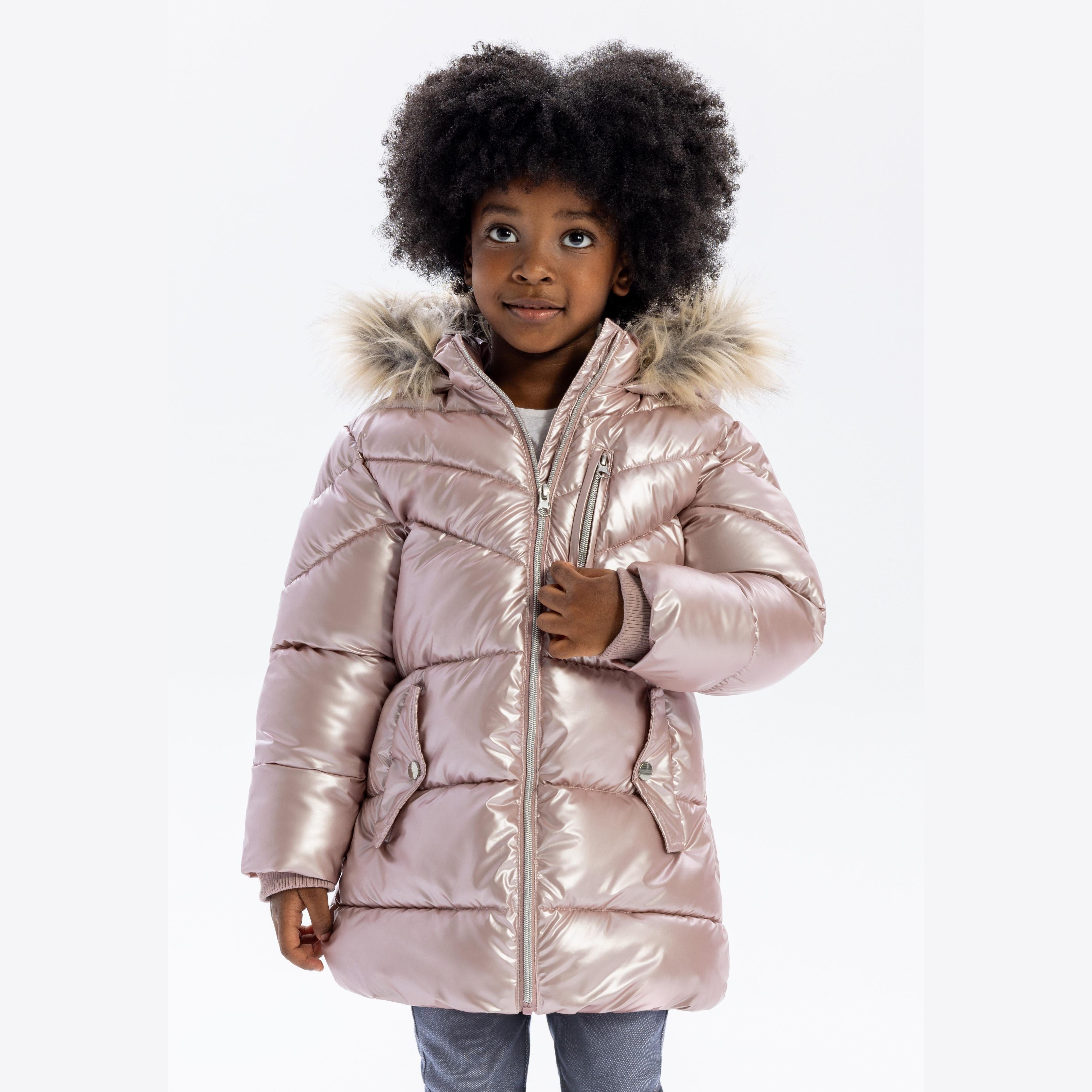 Young girl wearing glossy pink puffer coat with faux fur hood, smiling against white background, hands in pockets
