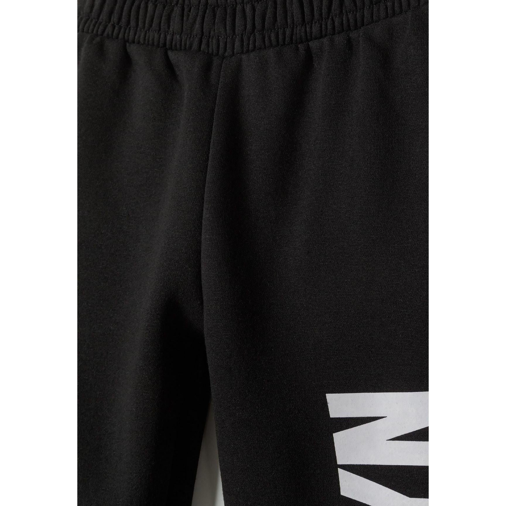 Close-up detail of black tracksuit joggers showing ribbed waistband and white text print on leg