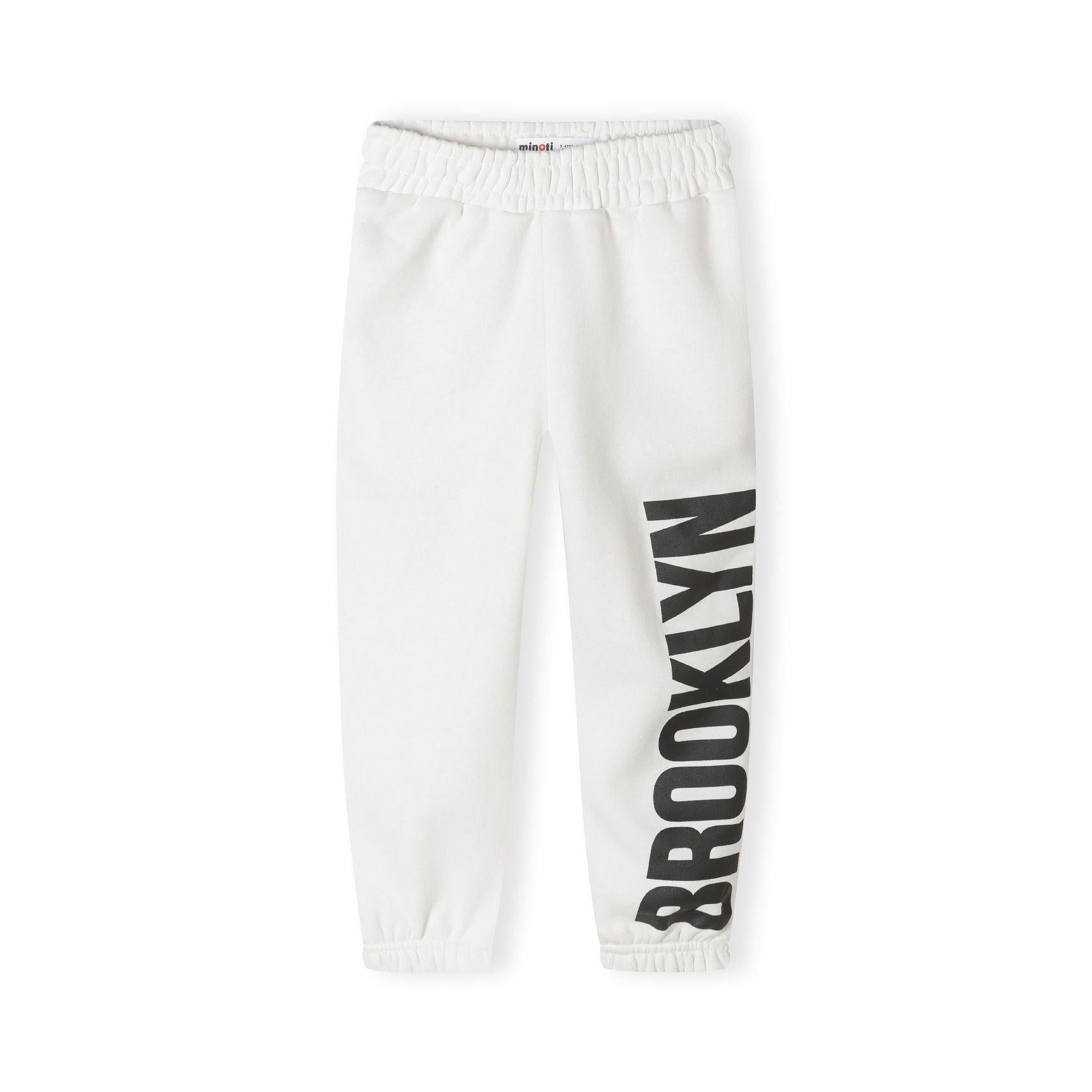 Close-up detail of white joggers showing black printed text on leg and elasticated waistband construction