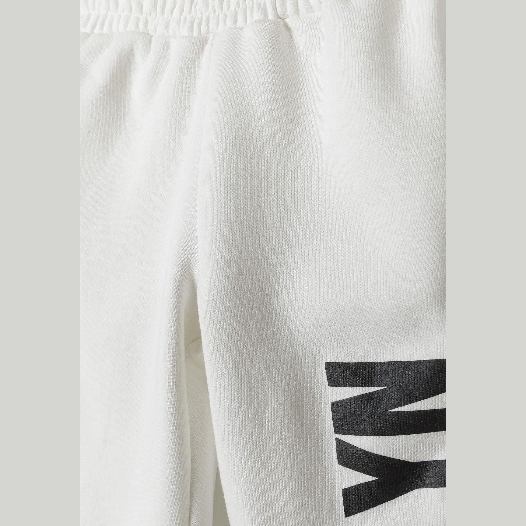 Close-up detail of white joggers showing black printed text on leg and elasticated waistband construction
