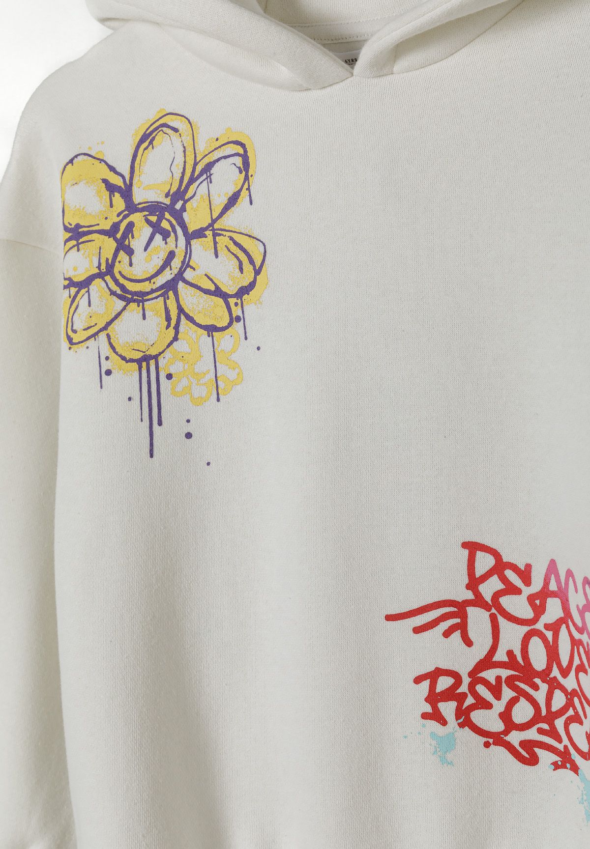 Detail of a girls hooded tracksuit in cream with printed flower and graffiti designs.