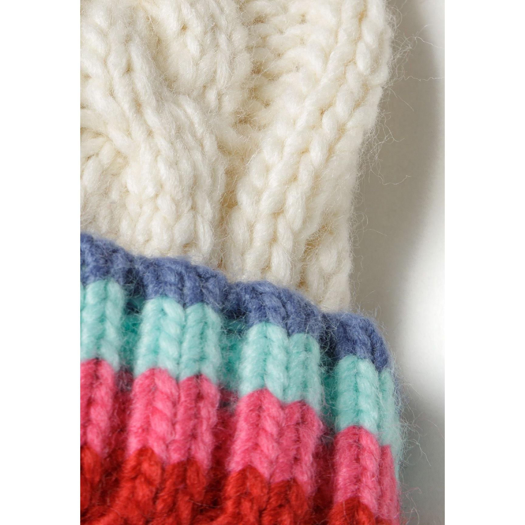 Detail of colourful pom pom in red, blue, mint and cream colours attached to cable knit hat