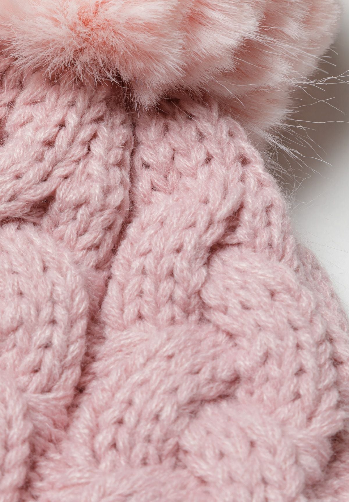 Light pink cable-knit bobble hat, pompom and cable detail.