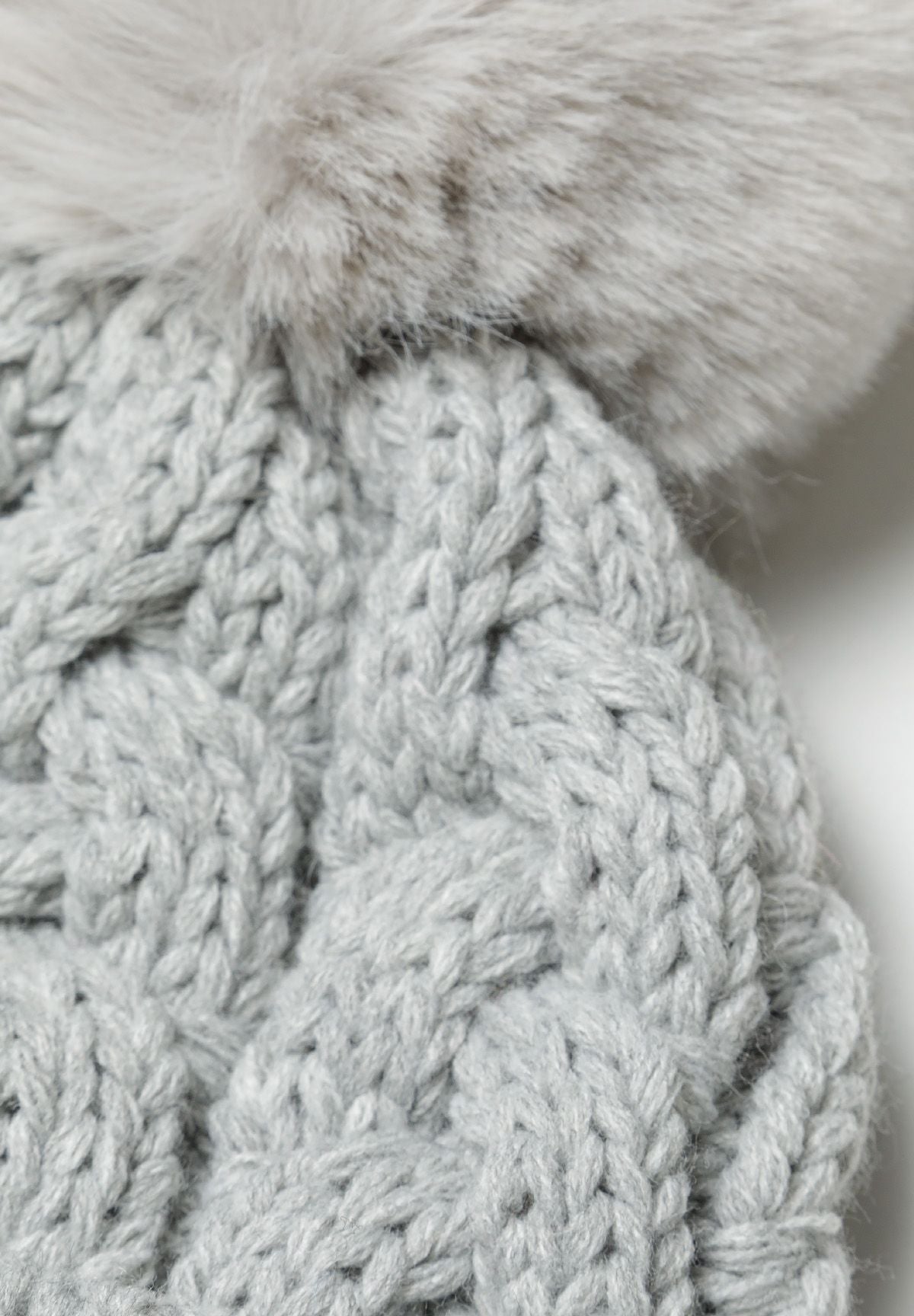 Light grey cable-knit bobble hat, pompom and cable detail.