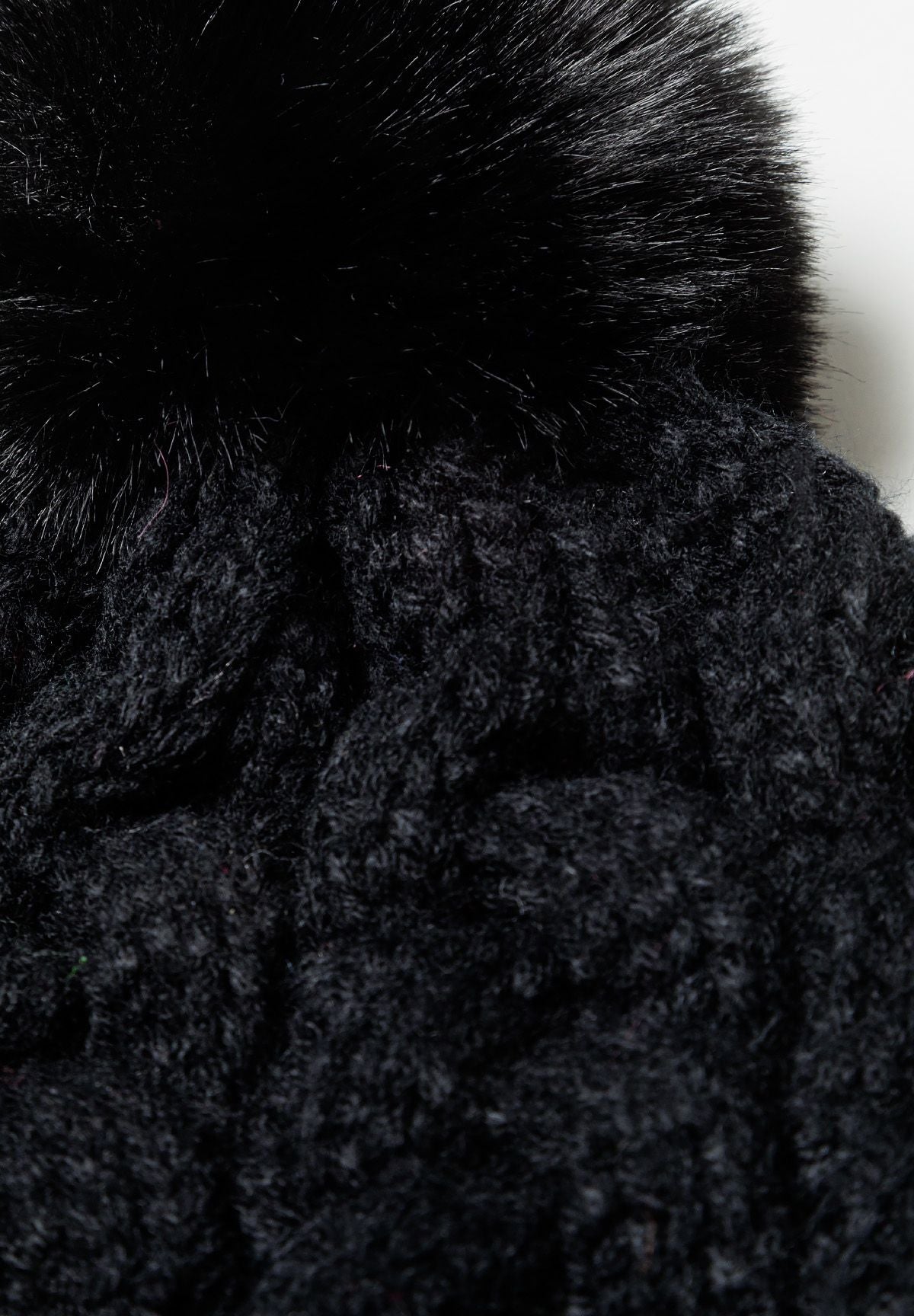 Close-up of a black knitted cable pom pom hat with a textured pattern.