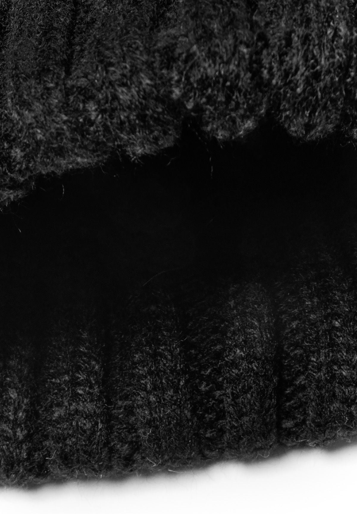 Detail of a black knitted cable pom pom hat for girls, showcasing the textured knit pattern.
