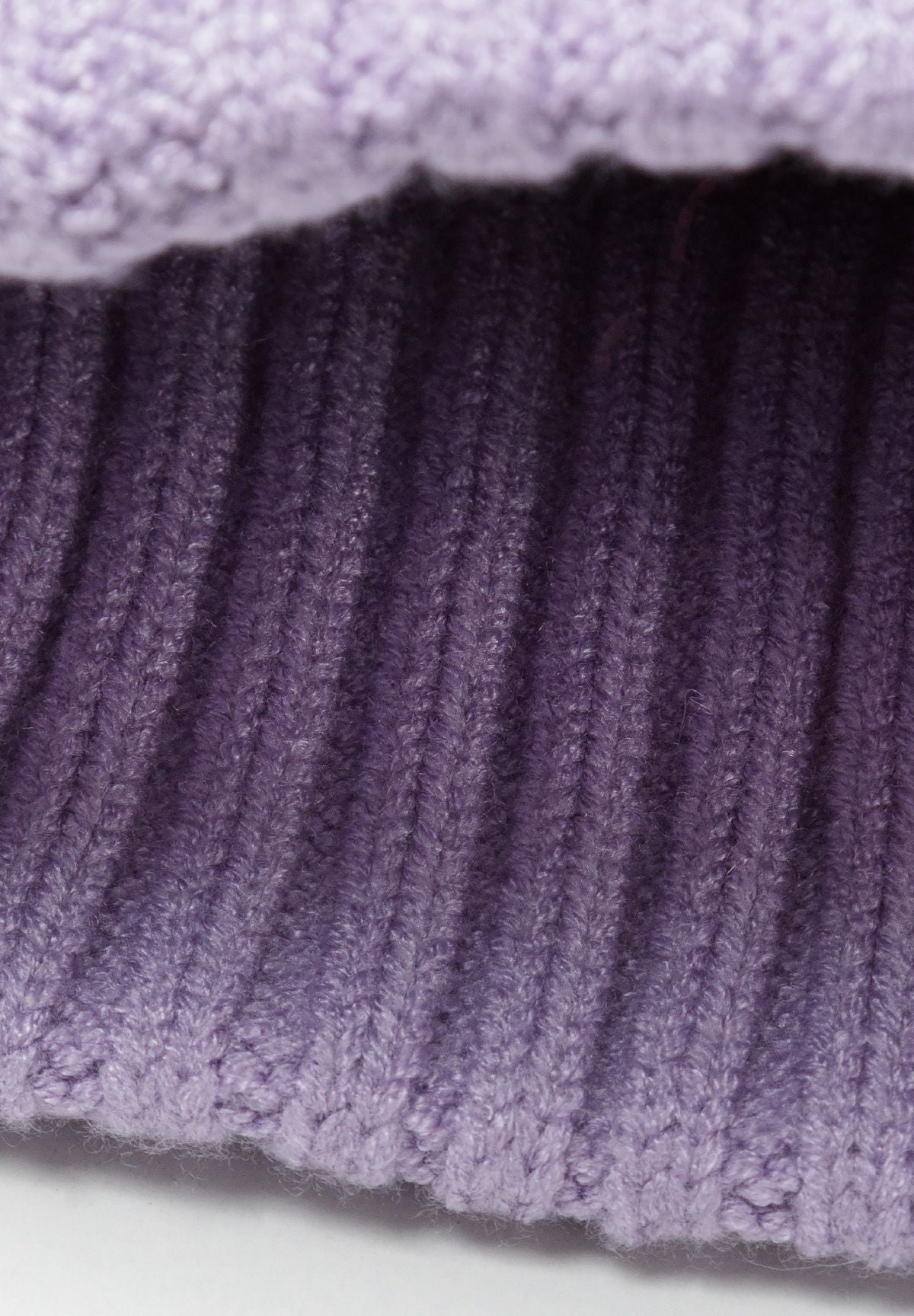 Close-up of a lilac knitted rib hat with a pom pom and ribbed edges.