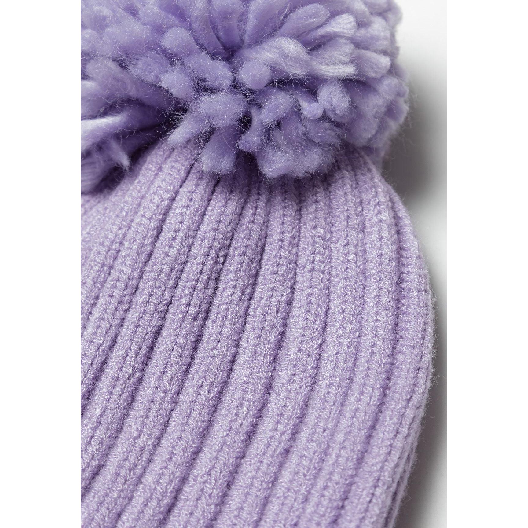 Close-up detail of lilac ribbed knit winter hat showing fluffy pom pom texture and vertical ribbed knit pattern