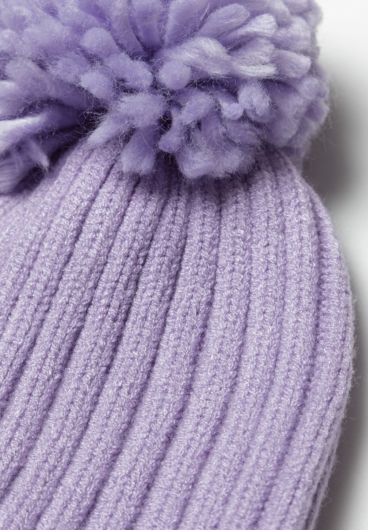 Close-up of a lilac knitted hat featuring a pom pom and ribbed texture.