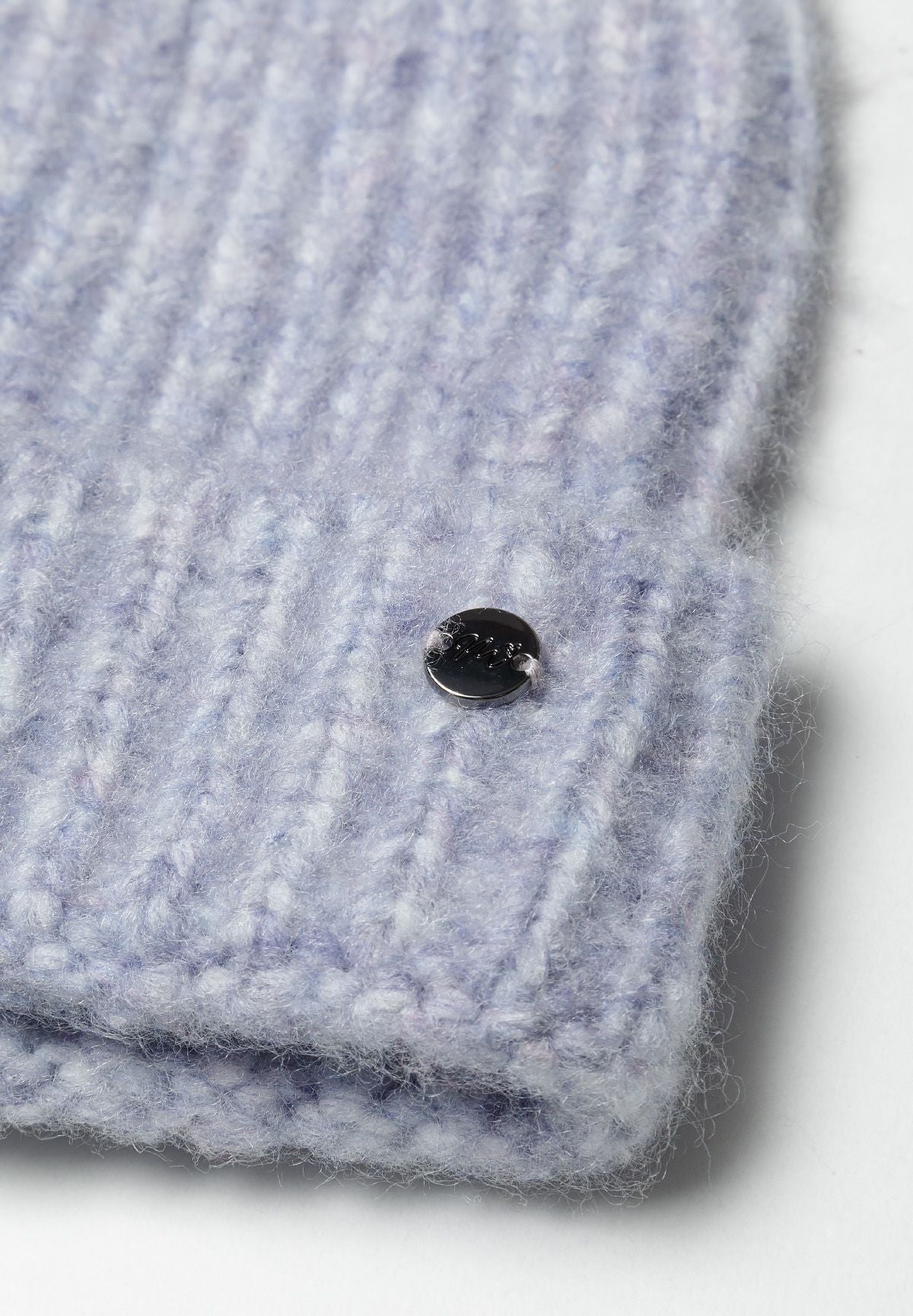 Detail of a knitted lilac yarn hat with a metal badge.