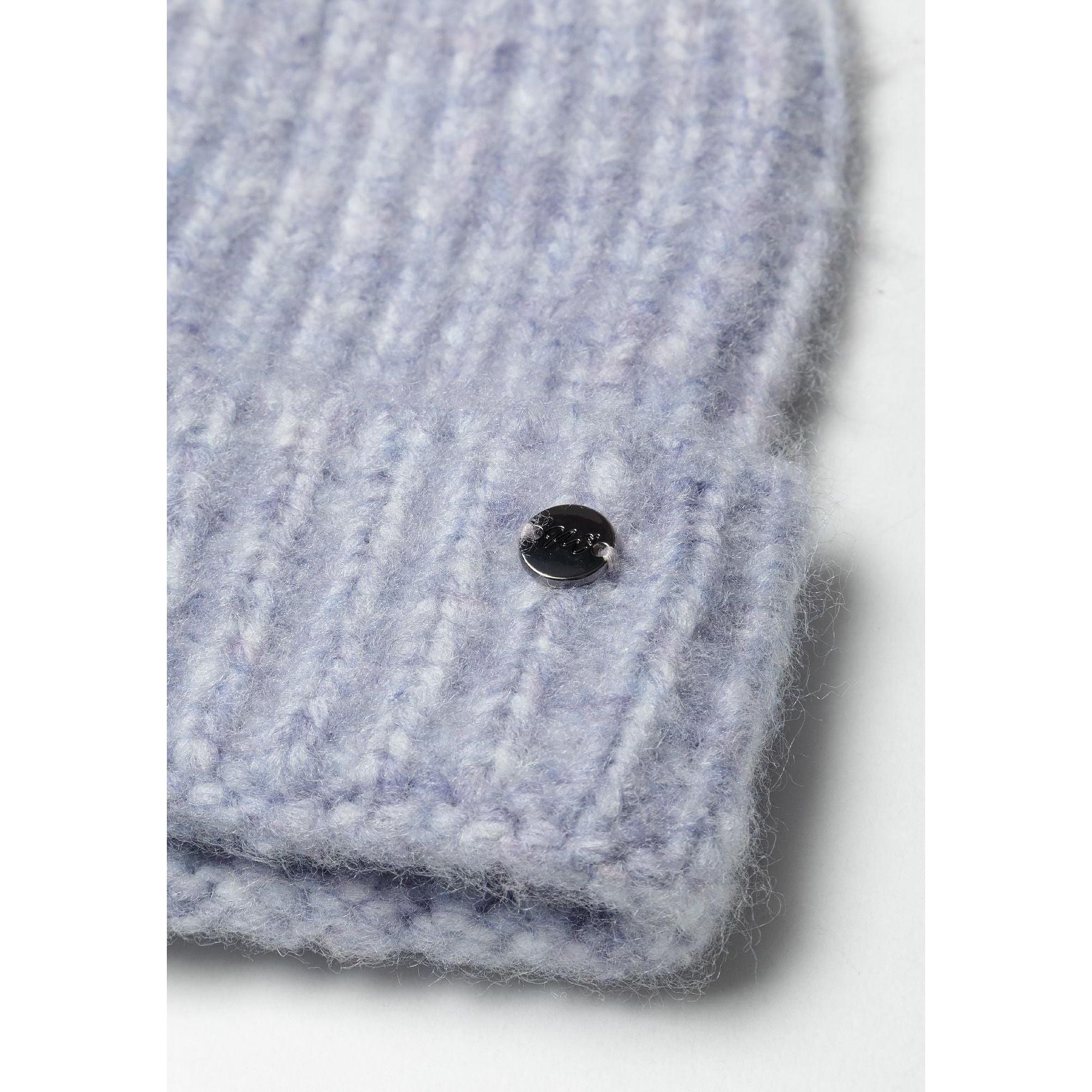 Close-up detail of lilac knitted beanie showing ribbed cuff texture and round metal badge embellishment