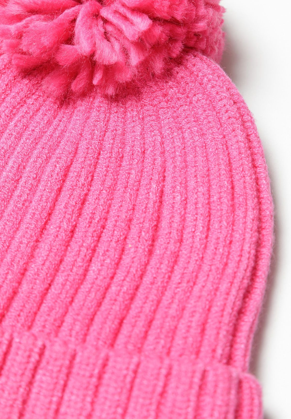 Close-up of a pink knitted hat with a pom pom and ribbed cuff.