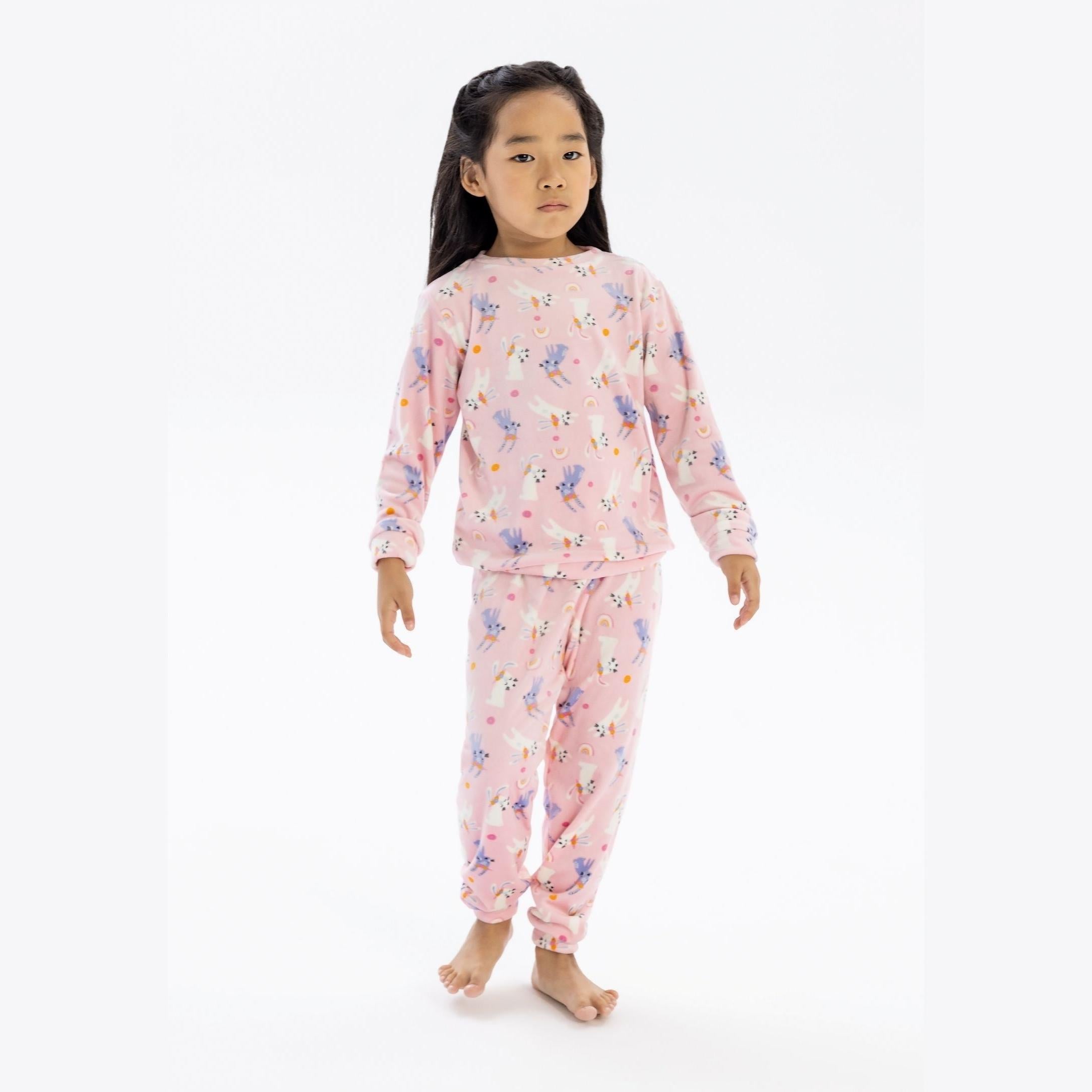 Young girl wearing pink velour pyjama set with unicorn print, standing against white background